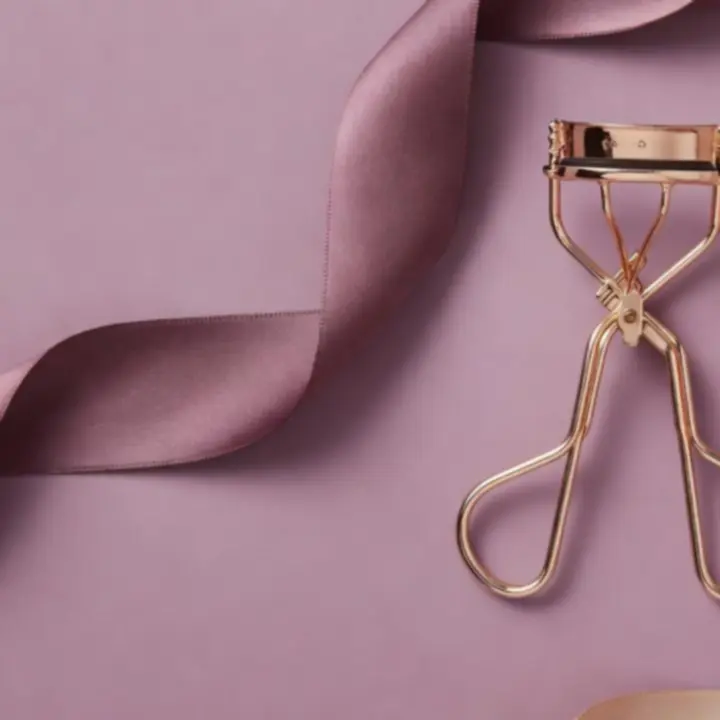 Luxurious eyelash curler presented in a flat-lay composition with soft beauty accents